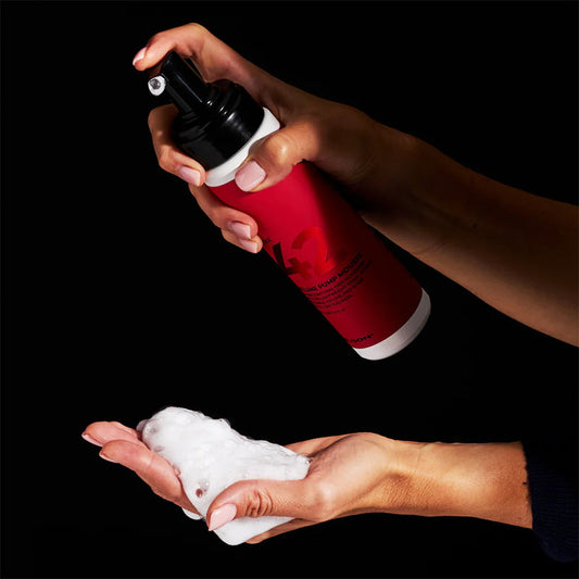 Flacone bianco con etichetta rossa con scritte nere e tappo spray nero, il quale viene erogato sul palmo di una mano.