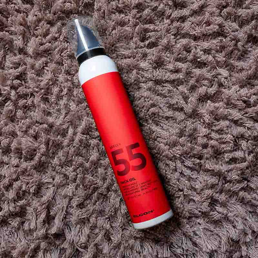 Flacone bianco con etichetta rossa con scritte nere ed erogatore nero con cappuccio trasparente steso su un tappeto marroncino.